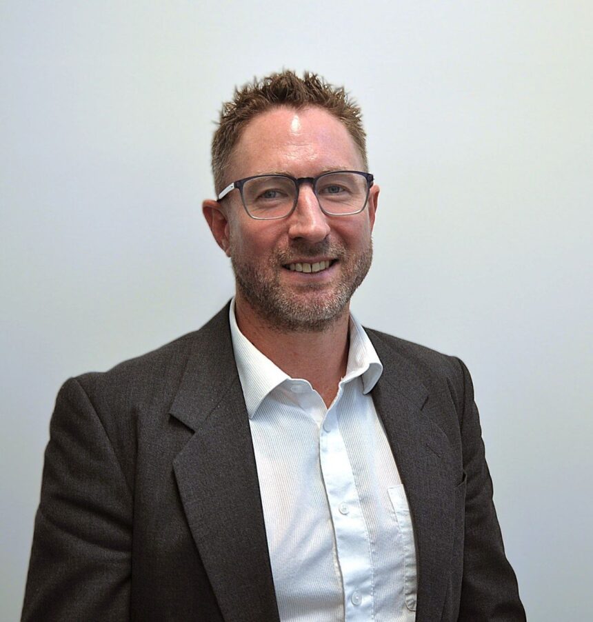 A professional portrait of a man in a blazer and white shirt.