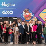 A large, diverse group of professional people posing in front of a Hasbro mural.