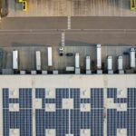 Aerial view of a warehouse facility with solar panels on the roof and parked trucks.