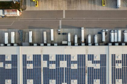 Aerial view of a warehouse facility with solar panels on the roof and parked trucks.