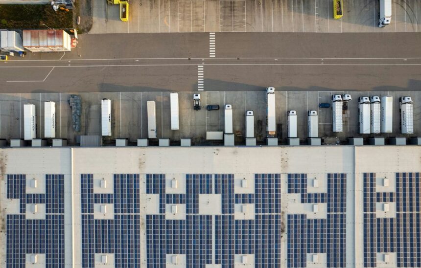 Aerial view of a warehouse facility with solar panels on the roof and parked trucks.