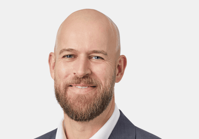 A smiling, bald man with a beard, wearing a gray suit and white shirt.