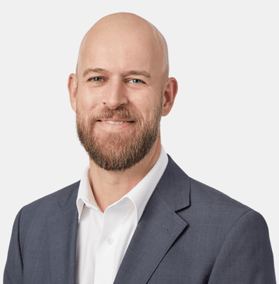 A smiling, bald man with a beard, wearing a gray suit and white shirt.