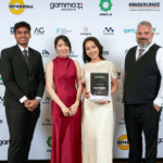 Four people stand in front of a branded backdrop for an award presentation ceremony.