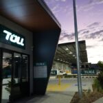 Modern Toll logistics facility entrance at dusk with a purple sunset sky.