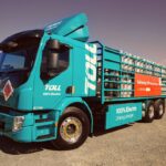 A turquoise Toll 100% electric truck carrying LPG cylinders parked outdoors.