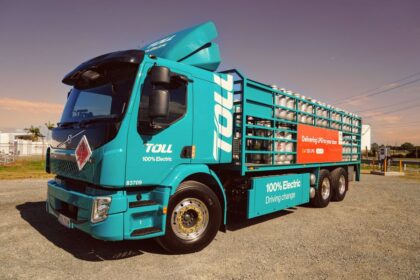 A turquoise Toll 100% electric truck carrying LPG cylinders parked outdoors.