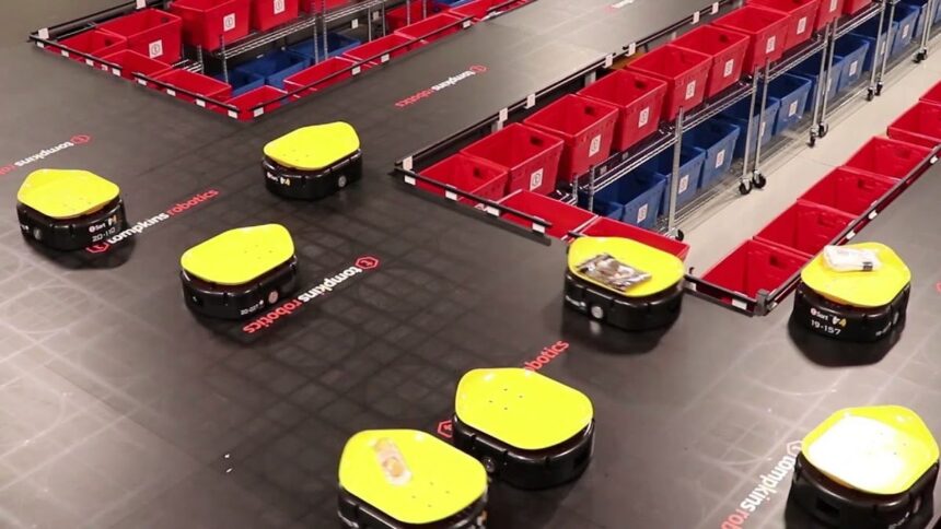 Yellow warehouse robots move packages past red and blue sorting bins on a track.