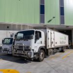 Two South West Healthcare trucks parked at a loading dock with a green building.