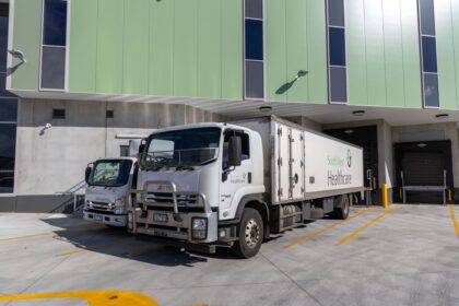 Two South West Healthcare trucks parked at a loading dock with a green building.
