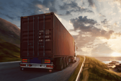 A cargo truck driving along a coastal road at sunset.