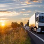 White semi-trucks driving on a highway during a beautiful golden sunset.