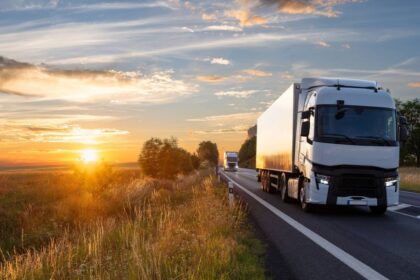 White semi-trucks driving on a highway during a beautiful golden sunset.