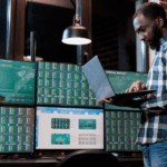A man in a plaid shirt analyzes stock market data on multiple computer screens.
