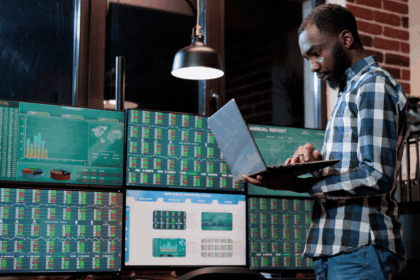 A man in a plaid shirt analyzes stock market data on multiple computer screens.