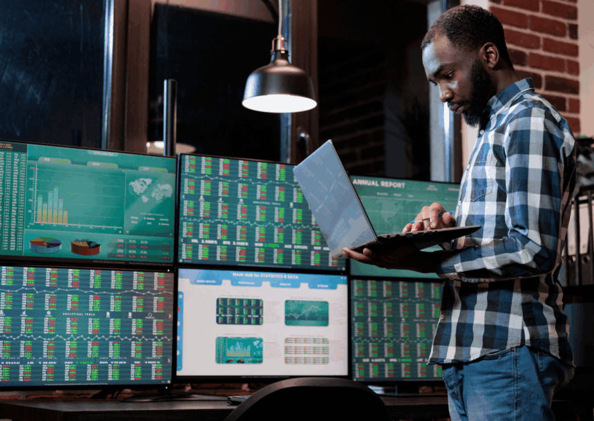 A man in a plaid shirt analyzes stock market data on multiple computer screens.