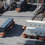 Automated guided vehicles transport shipping containers across a busy industrial port terminal.