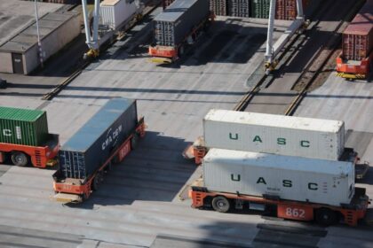 Automated guided vehicles transport shipping containers across a busy industrial port terminal.