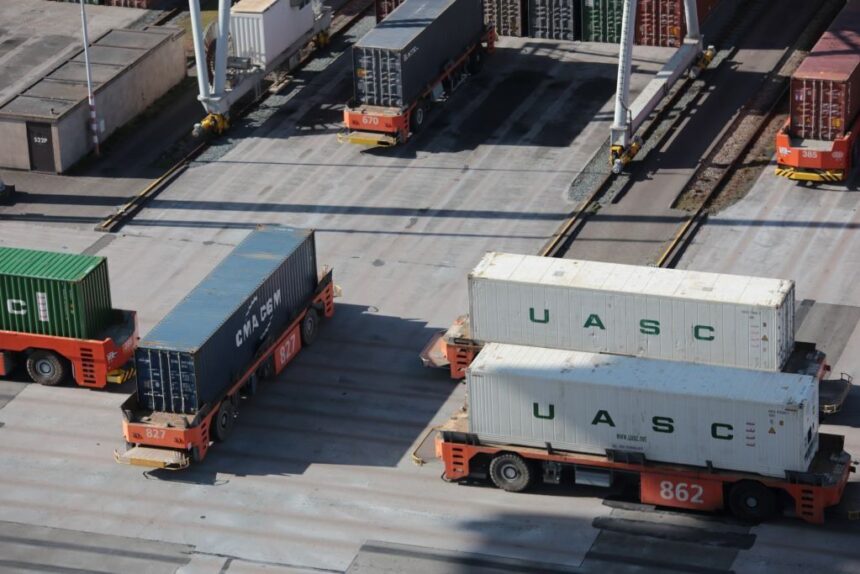 Automated guided vehicles transport shipping containers across a busy industrial port terminal.
