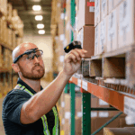 Warehouse worker wearing head-mounted technology scans a barcode on a cardboard box.
