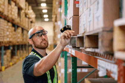 Warehouse worker wearing head-mounted technology scans a barcode on a cardboard box.