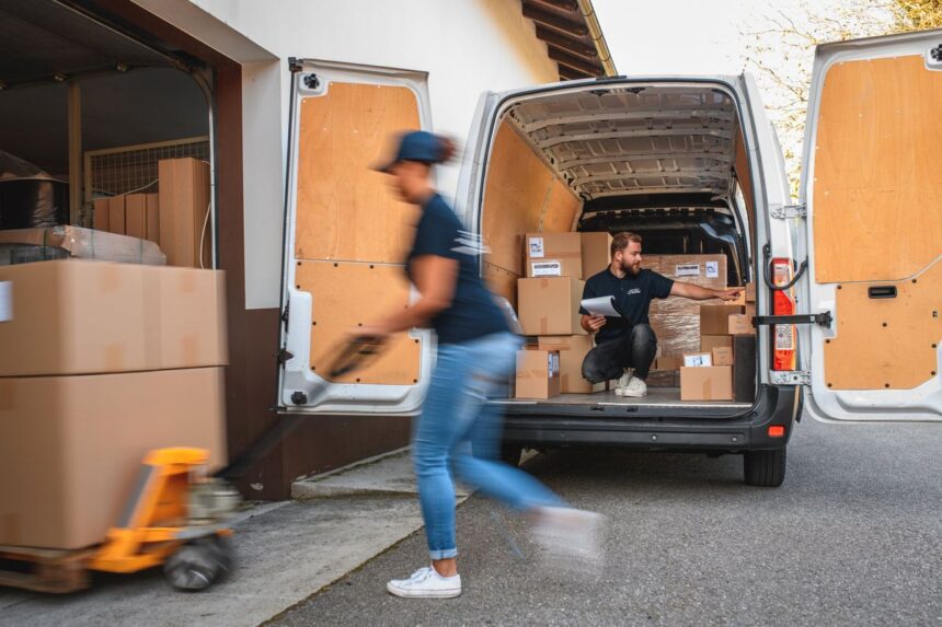 A worker uses a pallet jack while another organizes boxes inside a delivery van.