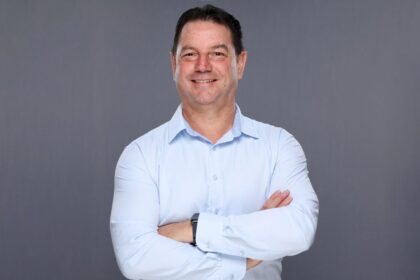 A middle-aged man in a light blue button-down shirt smiling with arms crossed.