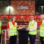 Four people in safety vests push a ceremonial button at a Coles warehouse opening.