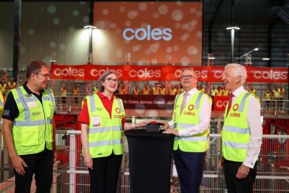 Four people in safety vests push a ceremonial button at a Coles warehouse opening.