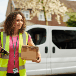 A delivery driver in a high-visibility vest holds a parcel and a digital tablet.