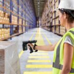 A warehouse worker scanning a pallet in a large distribution center aisle.