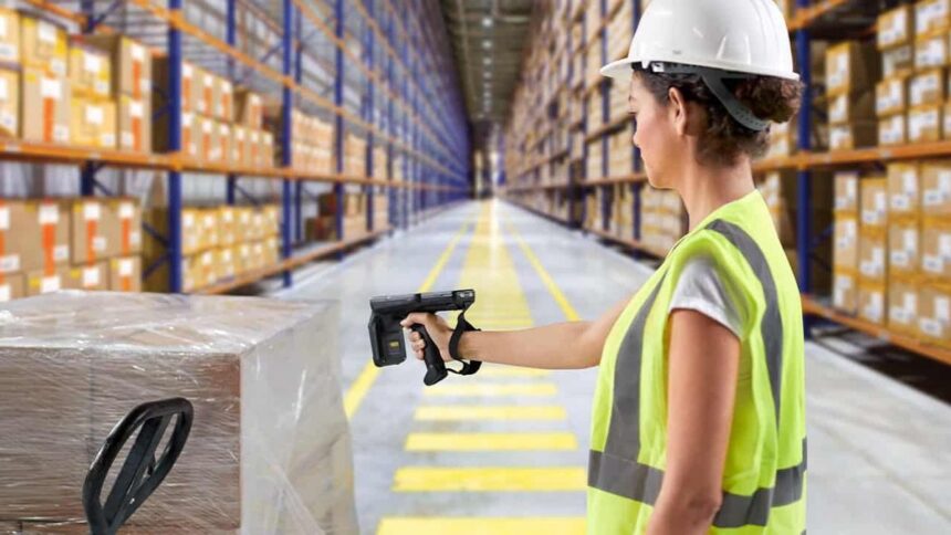 A warehouse worker scanning a pallet in a large distribution center aisle.
