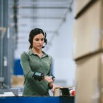 Warehouse worker wearing a headset and wrist-mounted scanner processing packages in a facility.