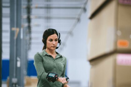 Warehouse worker wearing a headset and wrist-mounted scanner processing packages in a facility.