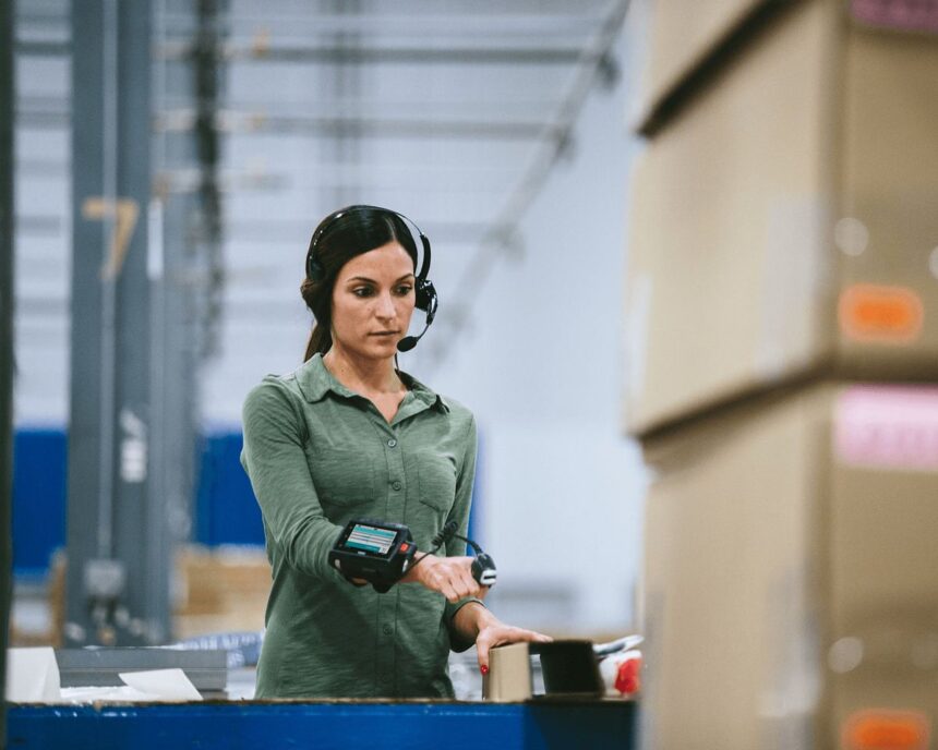 Warehouse worker wearing a headset and wrist-mounted scanner processing packages in a facility.