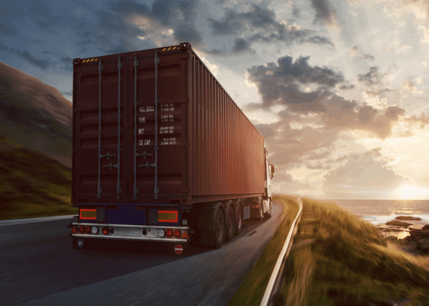 Semi-truck with cargo container driving on a coastal road at sunset.