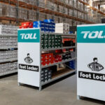 Toll and Foot Locker branded warehouse shelving filled with footwear stock, highlighting their extended ANZ logistics partnership.