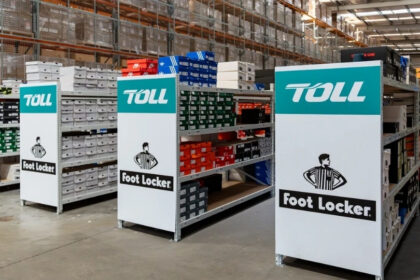 Toll and Foot Locker branded warehouse shelving filled with footwear stock, highlighting their extended ANZ logistics partnership.