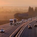 Alt text: Trucks and cars travelling along a highway at sunrise, representing transport, logistics and mobile infrastructure pressures.