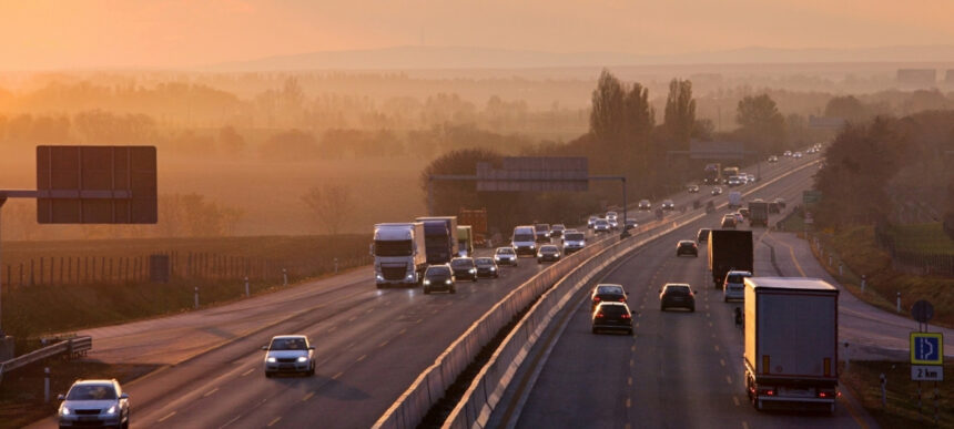 Alt text: Trucks and cars travelling along a highway at sunrise, representing transport, logistics and mobile infrastructure pressures.