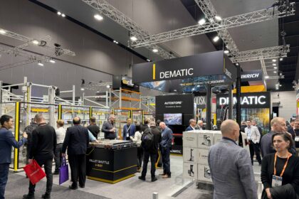 Visitors gather at the Dematic stand during CeMAT Australia 2026, where live demonstrations of warehouse automation technologies, including AutoStore and a 4-way pallet shuttle system, attract attendees exploring intelligent supply chain solutions. Large Dematic branding and exhibition displays are visible throughout the busy trade show floor.