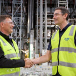 Dematic and Asahi Beverages representatives shaking hands inside an automated warehouse facility, marking a partnership milestone.