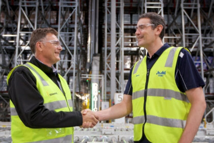 Dematic and Asahi Beverages representatives shaking hands inside an automated warehouse facility, marking a partnership milestone.