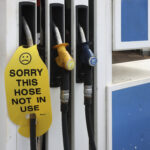 Close-up of a petrol station fuel pump with three fuel nozzles. A bright yellow cover on one nozzle displays a sad face icon and the words, "SORRY THIS HOSE NOT IN USE," indicating the pump is out of service.