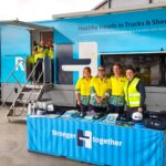 Healthy Heads in Trucks & Sheds mobile wellbeing truck with staff standing behind an information table displaying mental health resources for the transport and logistics industry.