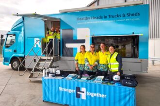 Healthy Heads in Trucks & Sheds mobile wellbeing truck with staff standing behind an information table displaying mental health resources for the transport and logistics industry.