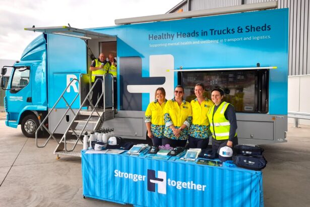 Healthy Heads in Trucks & Sheds mobile wellbeing truck with staff standing behind an information table displaying mental health resources for the transport and logistics industry.