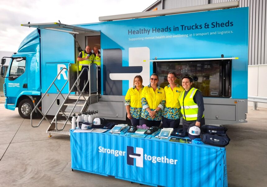 Healthy Heads in Trucks & Sheds mobile wellbeing truck with staff standing behind an information table displaying mental health resources for the transport and logistics industry.
