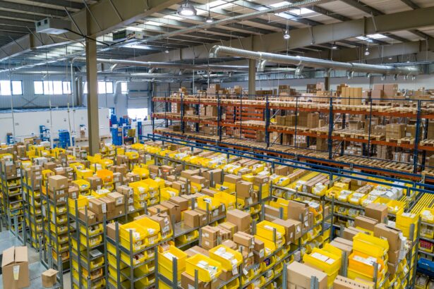 Wide view of a warehouse filled with shelving, yellow storage bins and cardboard boxes, with pallet racking and inventory storage extending across the facility.