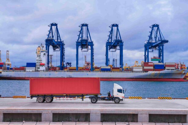 A container truck drives along a port terminal in front of a cargo ship and towering gantry cranes, illustrating the connection between road freight and international shipping.